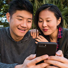Man and woman sitting closely at table outside looking at iPhone